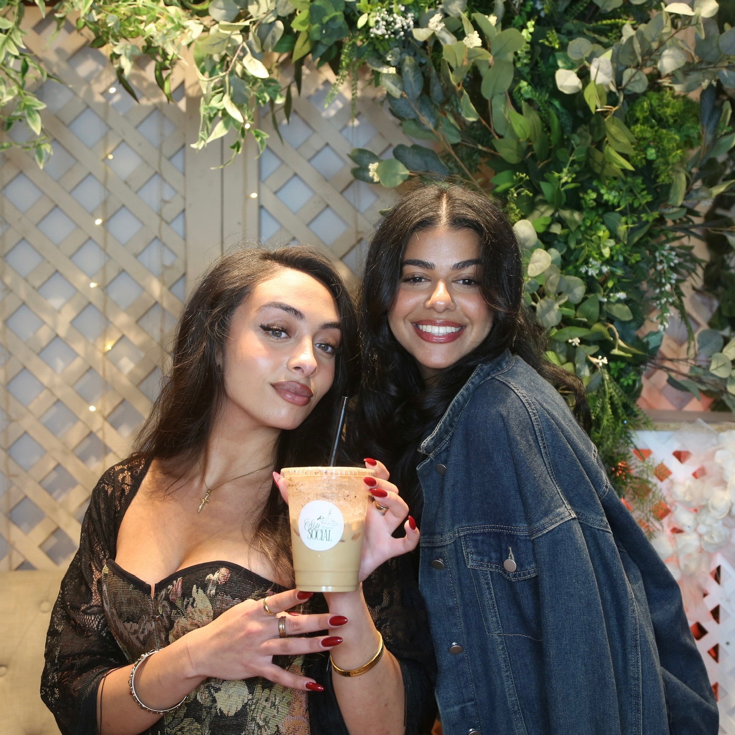 Guests posing with a signature Sip Social iced latte under a greenery arch
