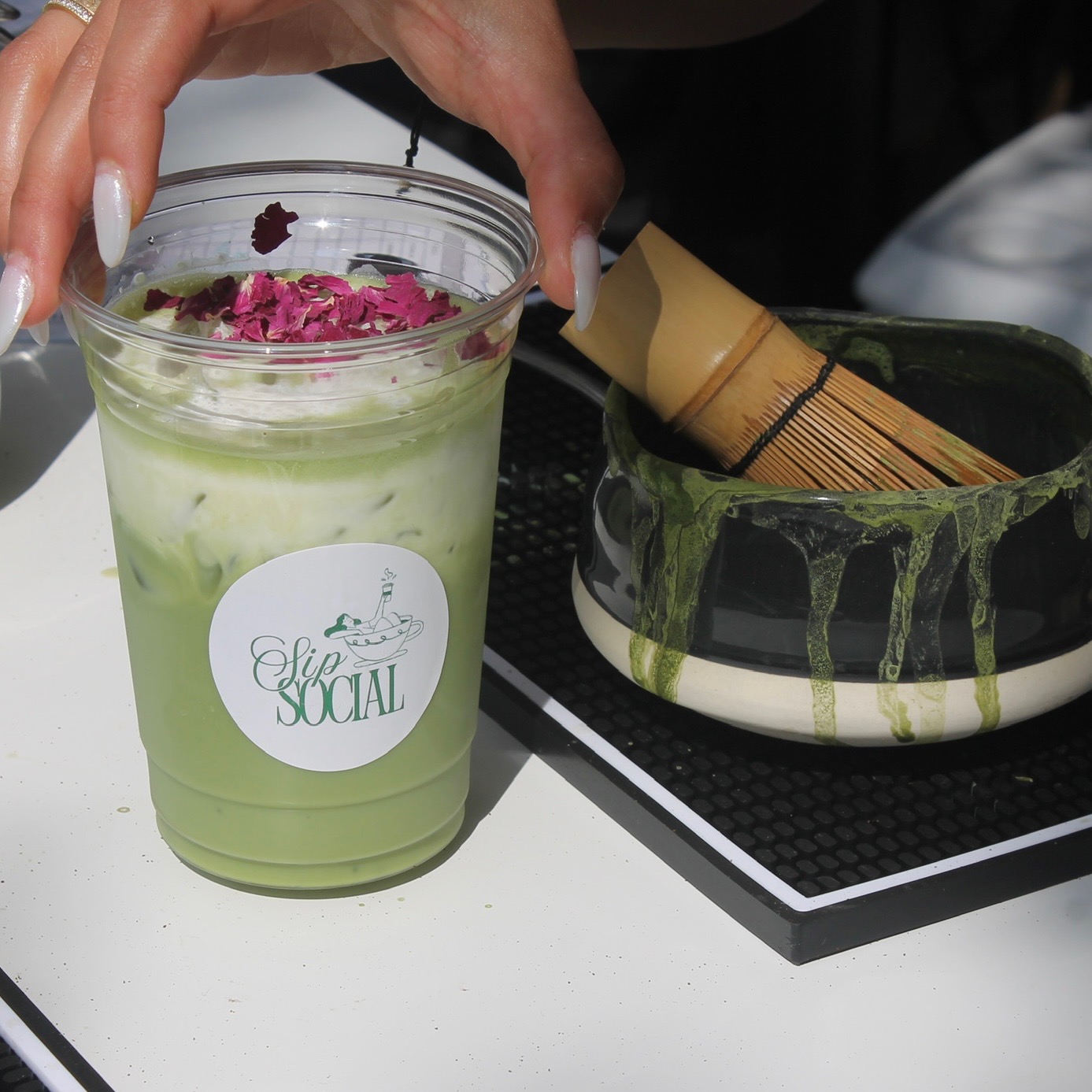 Iced matcha topped with rose petals beside a bamboo whisk